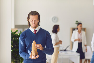 Office worker holding wooden rocket in hands in office