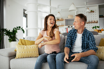 Obraz premium Husband and wife playing video game with joysticks in living room. Loving couple are playing video games at home