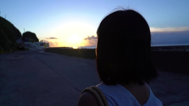 Camera following back of short haired female walking at dusk with sunset light behind her SLOW MOTION