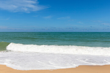 Fototapeta na wymiar Sandy beach with sea waves and blue sky background.