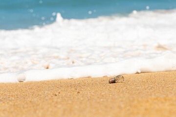 An old light bulb rests on the sandy beach and sea waves background.