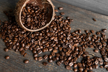Roasted arabica coffee beans scattered on a wooden table from a coconut. Fresh coffee beans.