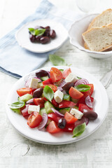 Simple salad with cherry tomatoes, feta cheese, kalamata olives, red pepper and fresh herbs. Bright wooden background. Close up. 