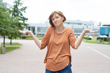 An adult redhead woman in casual clothes stands in the street spreading her arms and shrugging her...