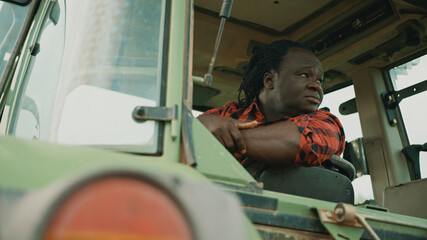 Tired young african farmer sitting in the tractor cabine and looking around. High quality photo © CameraCraft