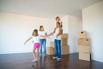 Sweet girls and their mom showing new flat to excited dad. Younger daughter riding on fathers neck. Apartment buying concept