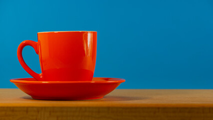 red cup with coffee on a plate stands on an oak table.