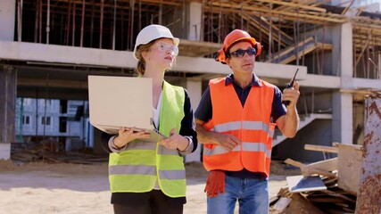 Young engineer lady with a laptop walking beside the foreman middle-aged they analyzing the plan of the construction site wearing safety helmets and goggles - Powered by Adobe