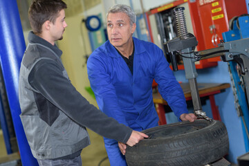 Obraz na płótnie Canvas apprentice mechanic and teacher retreading wheel in automotive workshop