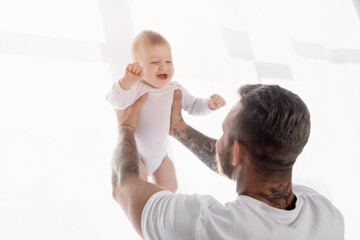 back view of young father holding excited baby boy in outstretched hands