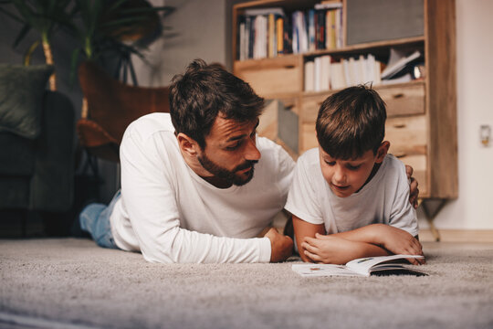 Young attractive father lying down on the floor with his son and studying with him.