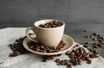 Coffee cup filled of fresh arabica or robusta coffee beans with scattered coffee beans on a linen textile and wood table.