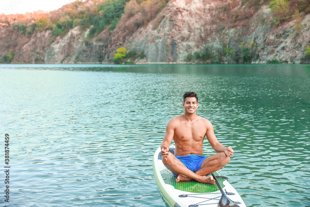 Wall mural Young man practicing yoga on paddle board in river