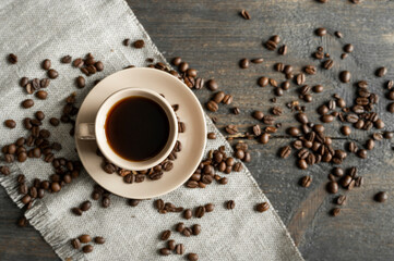 Coffee cup with roasted coffee beans on wooden table background. Mug of black coffe with scattered...