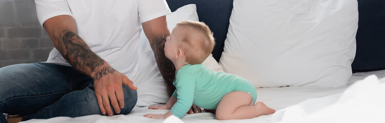 panoramic concept of infant boy in baby romper crawling on bed near father
