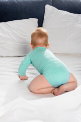 back view of infant kid in baby romper crawling in bed