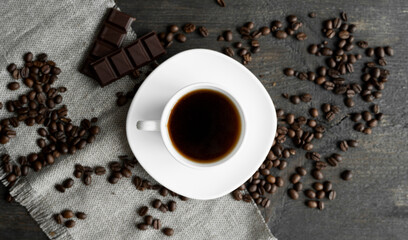 Coffee cup with cookies and chocolate with scattered coffee beans on linen and wooden table background. Mug of black coffee.