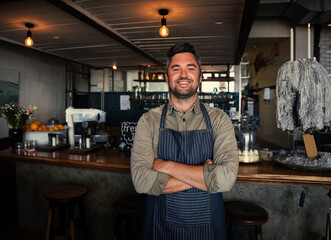 Smiling waiter standing with cross-arms happily working in cafe