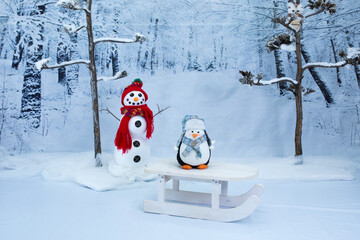 Christmas background with snowy forest, snowman and a toy penguin