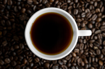 White cup of coffee with roasted coffee beans background. Mug of black coffee.