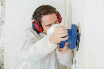 Fototapeta na wymiar builder wearing dust mask using a sander on wall surface