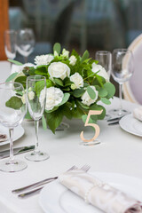 A white and green bouquet of flowers in a golden vase stands on a festive table close-up. Number five. Served table