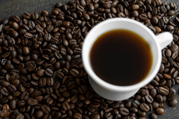 White cup of coffee with roasted coffee beans background. Mug of black coffee.