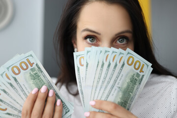 Young businesswoman is holding many american dollars in her hands, covering her face. Disbursement of loans social guarantees concept.