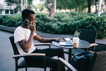 Young guy using laptop and talking on phone in cafeteria