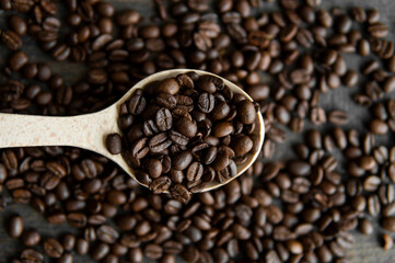 Fresh roasted arabica coffee beans in a wooden spoon and scattered coffee beans on a wooden table.