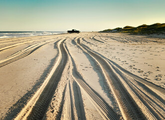 Fototapeta premium Sand tracks on the beach with black truck