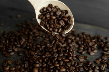Fresh roasted arabica coffee beans falling from a oaken spoon on a wooden table.
