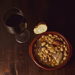 Tradicional guiso de judías español con vino y pan sobre mesa de madera oscura