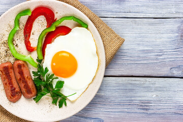 sunny side up. Fried eggs with sausages and vegetables on a light wooden table. Top view
