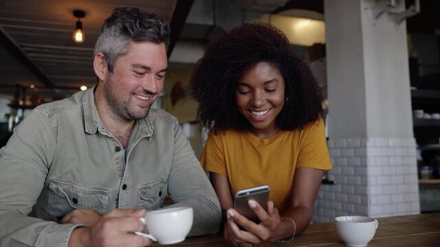 Cute couple looking at vacation pictures sipping coffee in funky cafe 