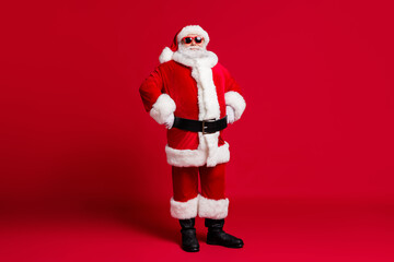 Full length photo of retired old man grey beard self-assured hands hips prepare deer for trip wear santa costume gloves coat belt sunglass headwear black boots isolated red color background