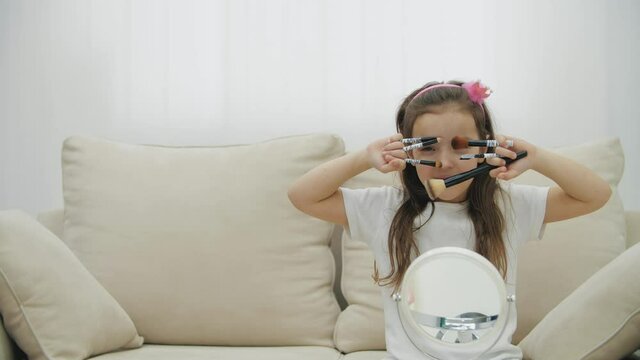 4k slowmotion video of smiling chils girl holding cosmetic brushes in the living room.