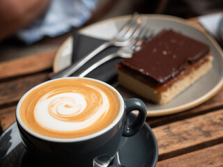 cup of coffee with chocolate brownie on a plate. Coffee in focus, brownie blurry in background