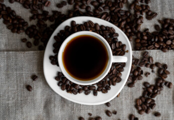 Coffee cup with roasted coffee beans on linen background. Mug of black coffe with scattered coffee beans. Fresh coffee beans.