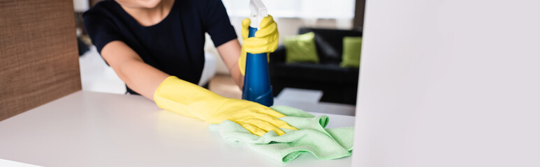 horizontal crop of maid in rubber gloves holding spray bottle and rag while cleaning shelf in hotel room
