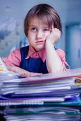 Humorous portrait of tired and exhausted  business child girl in office with a lot of documents. Selective focus on eyes.