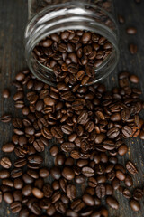 Roasted fresh arabica coffee beans scattered on a table from a little jar on a wooden table. Fresh coffee beans.