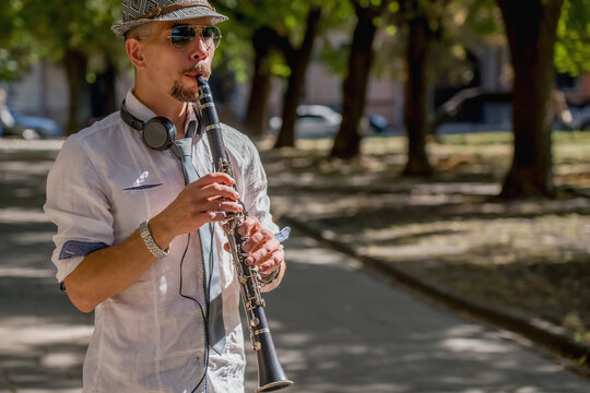 Musician wearing in titfer playing music with clarinet on a city sidewalk.