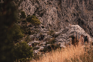 Group of people seen from behind hiking above the city of Omis, going towards the Fortica castle. Cold autumn day, following a small path surrounded by bushes and rocks