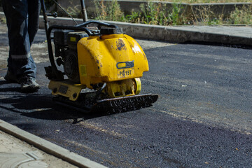 Obraz premium Vibratory plate for asphalt. Pothole repair process. Asphalt compaction machine. New asphalt