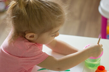 Fototapeta premium little girl painting with paintbrush and colorful paints.