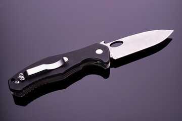 open folding pocket knife with textured black composite plastic cover plates on steel handle isolated on dark background with reflection on glossy surface.
