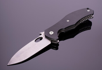 open folding pocket knife with textured black composite plastic cover plates on steel handle isolated on dark background with reflection on glossy surface.