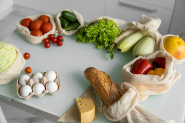 Vegetables, fruits, eggs in reusable eco cotton bags on table. Zero waste shopping concept. Plastic free items. Multi-use, reuse, recycle. Eco friendly canvas grocery bag with tomatoes, pepper, bread.