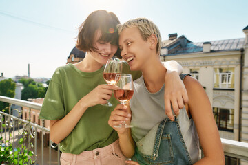 Two cheerful women holding glass of wine, hugging while having party, celebrating anniversary on...
